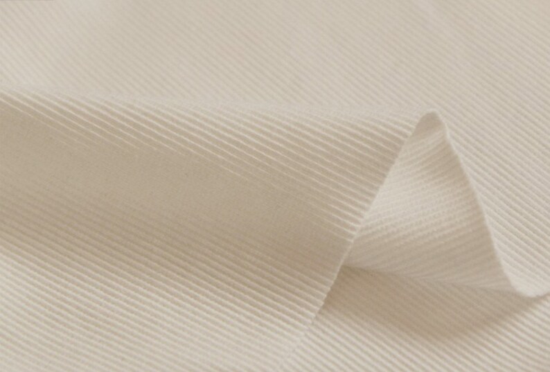 May include: Close-up of a white ribbed fabric with a slight fold. The fabric has a smooth, soft texture.