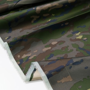 May include: Close-up of a camouflage fabric with a green, brown, and blue pattern. The fabric has a white edge.