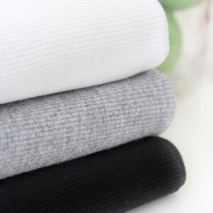 May include: Three ribbed fabric swatches stacked on top of each other. The top swatch is white, the middle swatch is gray, and the bottom swatch is black.
