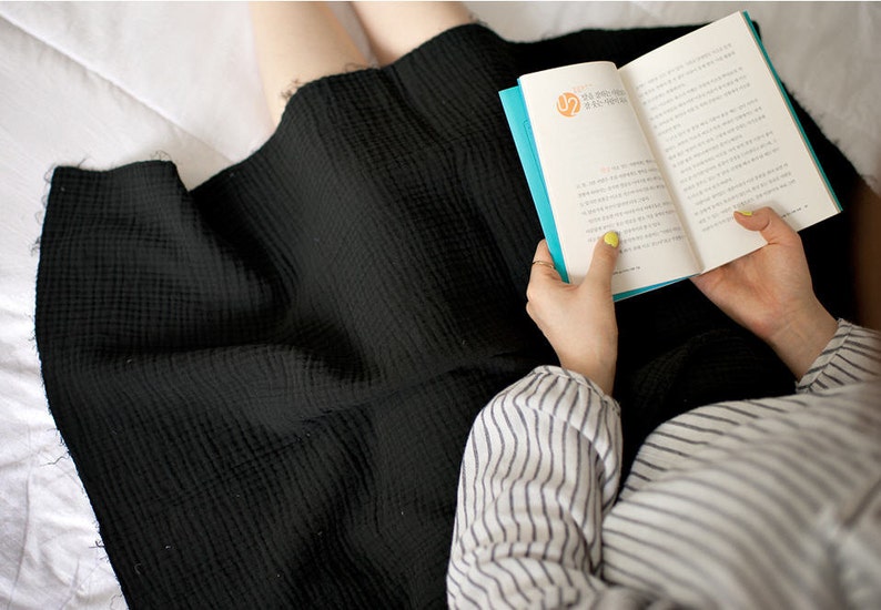 Op de afbeelding: Een persoon draagt een zwarte rok en een gestreept shirt en leest een boek met een blauwe kaft. Het boek heeft Koreaanse tekst op de kaft.