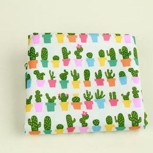 Puede incluir: Tela blanca con un patrón repetido de plantas de cactus verdes en macetas de colores. Las plantas de cactus son de varias formas y tamaños.