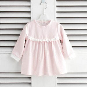 May include: A pink and white striped long-sleeved dress with a white ruffle trim around the neckline.