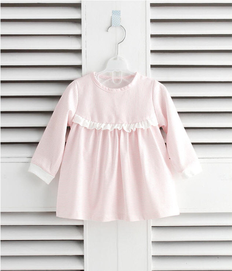 May include: A pink and white striped long-sleeved dress with a white ruffle trim around the neckline.