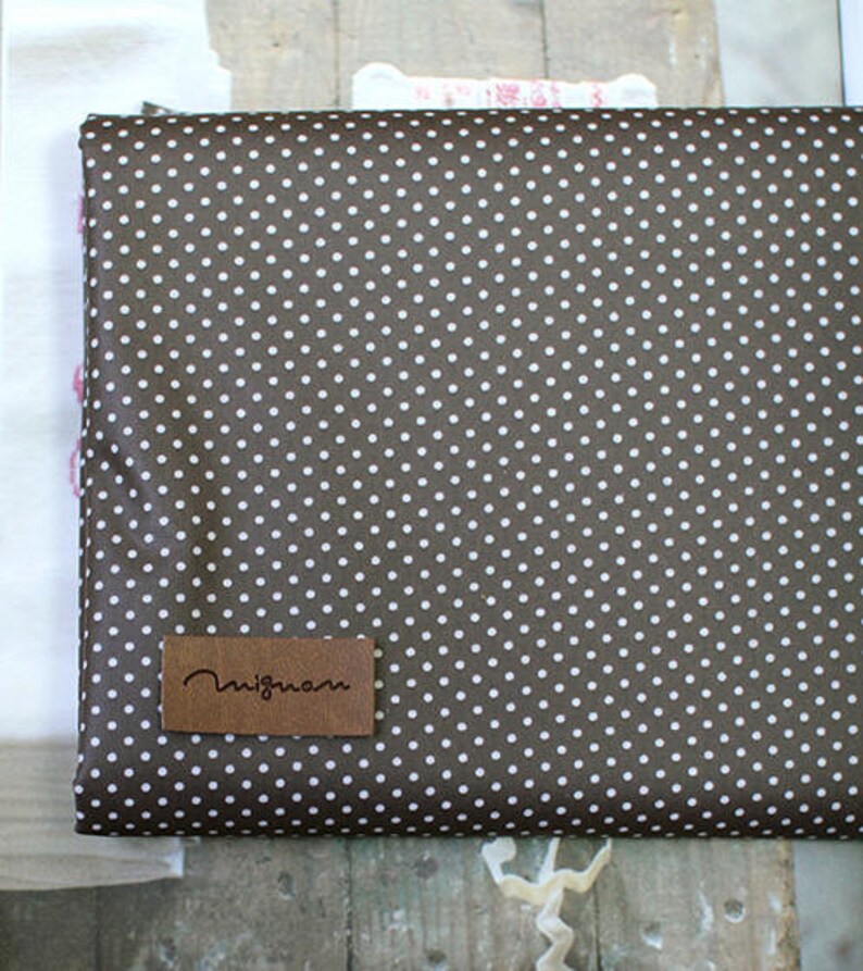 May include: Brown fabric with a white polka dot pattern. The fabric has a brown leather label with the text "nigma" on it.