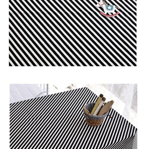 Puede incluir: Mantel de mesa a rayas blancas y negras con un patr&oacute;n diagonal. El mantel est&aacute; colocado sobre una mesa con una silla blanca y una cesta de objetos de madera.
