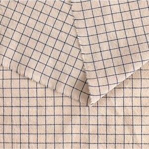May include: Close-up of a beige fabric with a black and white checkered pattern. The fabric is folded in half, showing the pattern on both sides.