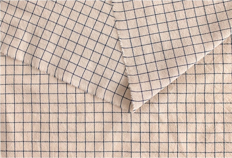 May include: Close-up of a beige fabric with a black and white checkered pattern. The fabric is folded in half, showing the pattern on both sides.
