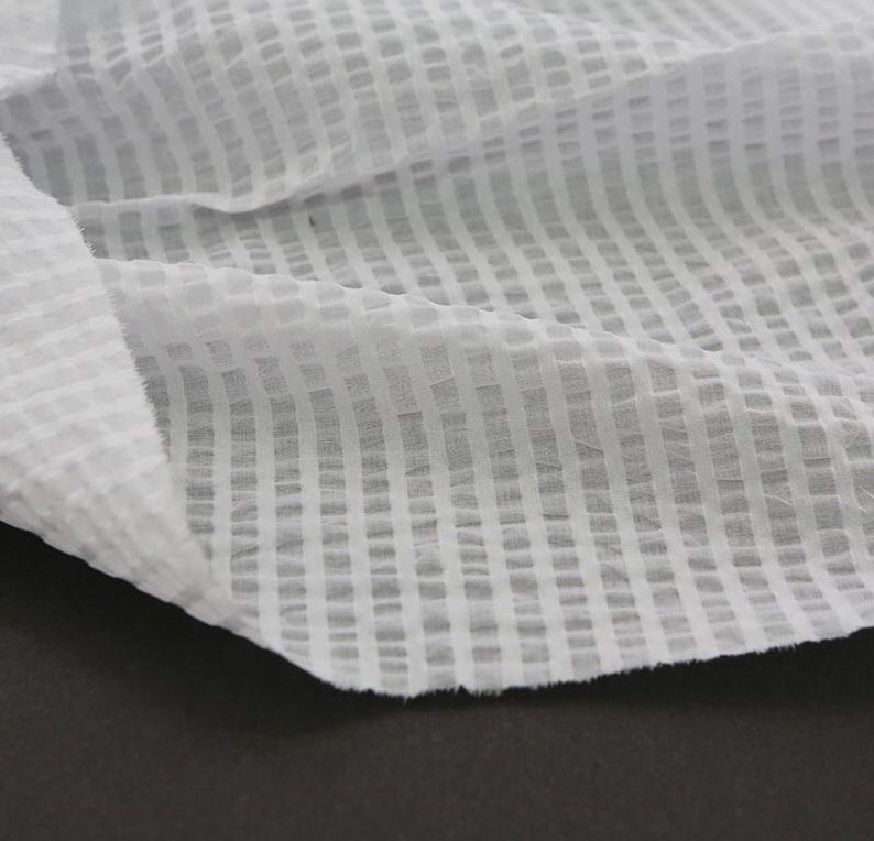May include: White cotton fabric with a grid pattern. The fabric is sheer and has a slightly textured surface.