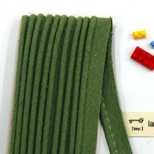 Op de afbeelding: Groene katoenen stofbies met een geplisseerde textuur en een witte gestikte rand.