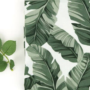 Puede incluir: Tela verde y blanca con un patrón de hojas tropicales. Las hojas son grandes y tienen una textura realista.