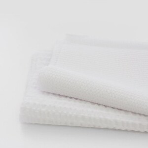 May include: Two white waffle weave towels folded on top of each other. The towels are soft and fluffy.