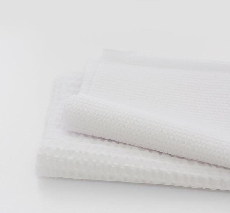 May include: Two white waffle weave towels folded on top of each other. The towels are soft and fluffy.