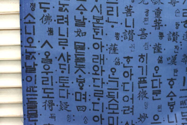 May include: A blue fabric with black Korean characters printed on it. The characters are in a variety of sizes and styles. The fabric is a light blue color and has a slightly textured surface.