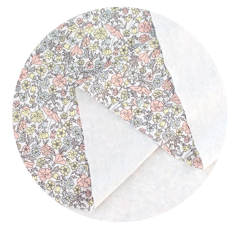 May include: A white fabric with a floral pattern in shades of pink, yellow, and grey. The fabric is folded in half, showing the white side on the bottom.