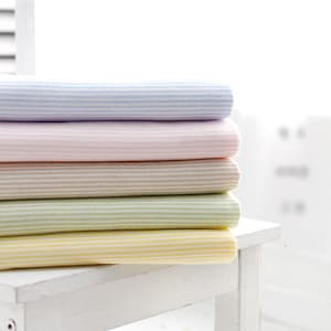 May include: A stack of five striped fabric swatches in pastel colors, including light blue, pink, beige, green, and yellow. The swatches are folded and stacked on a white table.