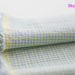 Pu&ograve; includere: Un pezzo di stoffa piegato con un motivo a quadri blu e gialli. La stoffa ha un bordo sfrangiato e il testo "Sky Yellow" &egrave; scritto in rosa sopra la stoffa.
