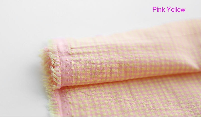 Pu&ograve; includere: Tessuto gingham rosa e giallo con un bordo sfrangiato. Il tessuto &egrave; piegato a met&agrave; e il testo "Pink Yellow" &egrave; visibile in alto a destra.