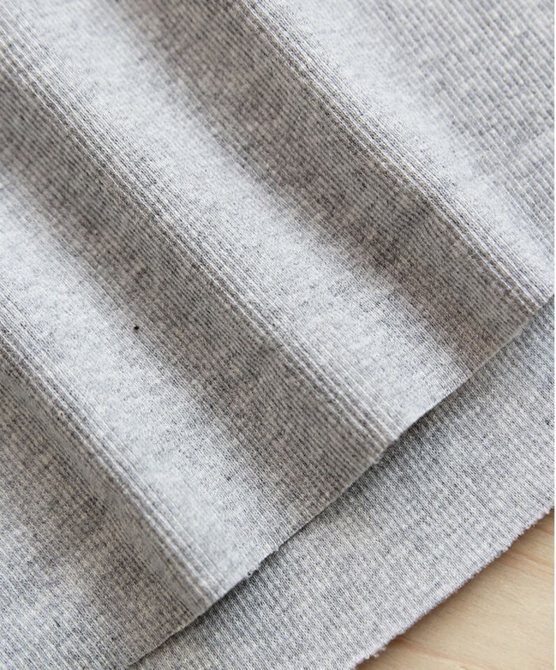 May include: Close-up of a gray ribbed fabric. The fabric is folded over itself, showing the texture of the material.
