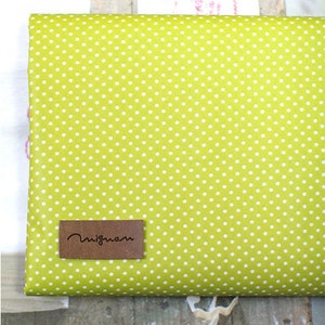 May include: A green fabric with white polka dots and a brown leather label that says "Migmom".