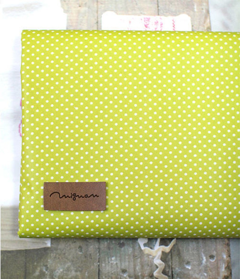May include: A green fabric with white polka dots and a brown leather label that says "Migmom".