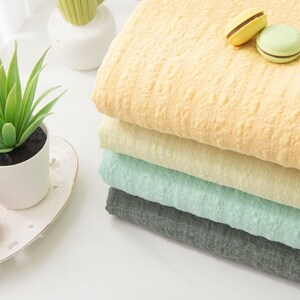 May include: A stack of four fabric swatches in different colors: yellow, light yellow, light green, and gray. The fabric has a textured, crinkled look.