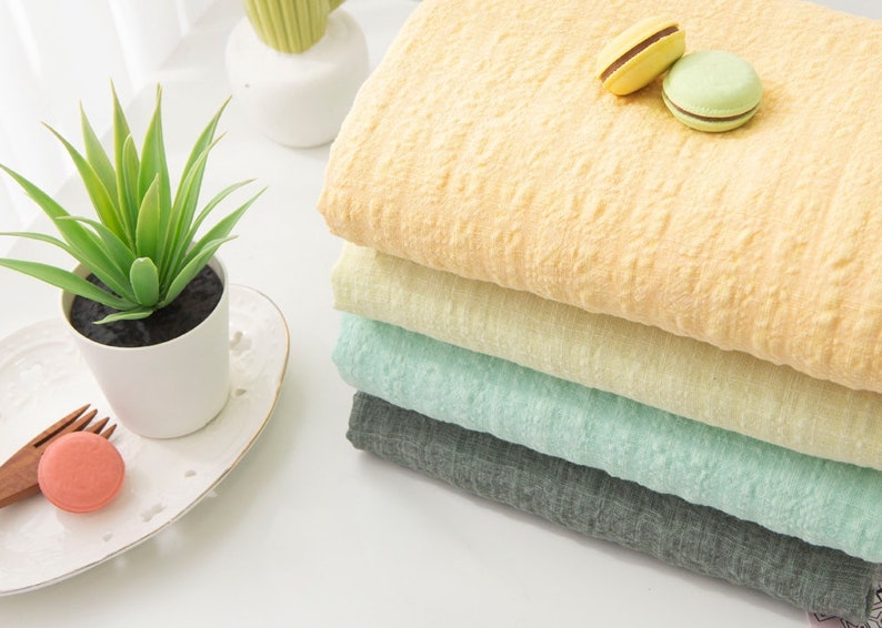 May include: A stack of four fabric swatches in different colors: yellow, light yellow, light green, and gray. The fabric has a textured, crinkled look.