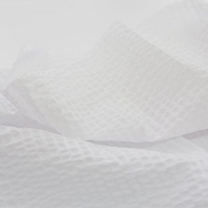 May include: White waffle weave fabric with a textured surface. The fabric is folded and draped, creating soft folds and curves.