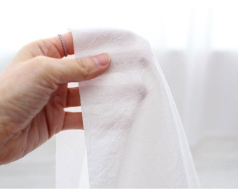 Puede incluir: Primer plano de una tela blanca, mostrando su textura y caída. La tela está sostenida en una mano, con un anillo en el dedo.