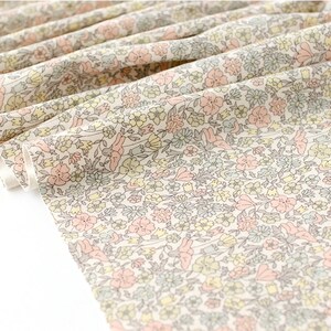 May include: A white fabric with a small-scale floral print in shades of pink, yellow, and green. The fabric is folded and the edges are visible.