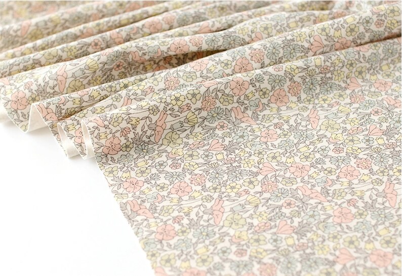 May include: A white fabric with a small-scale floral print in shades of pink, yellow, and green. The fabric is folded and the edges are visible.