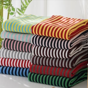 May include: A stack of striped fabric swatches in various colours, including yellow, red, pink, black, grey, blue, and green. The fabric is folded neatly and arranged in a pile.
