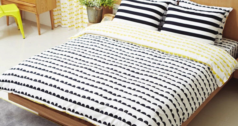 May include: A white and black striped duvet cover with a black and white patterned duvet insert. The duvet cover has a yellow trim. The duvet is on a wooden bed frame.