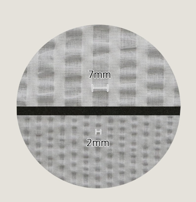 May include: Close-up of a gray fabric with two different weave patterns. The top pattern has larger squares and the bottom pattern has smaller squares. The top pattern is labeled "7mm" and the bottom pattern is labeled "2mm".