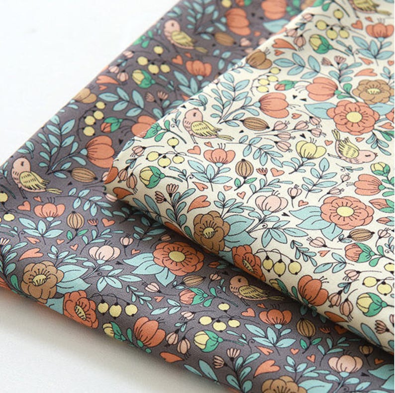 May include: Two pieces of fabric with a floral pattern. One fabric is a light beige with a light blue, pink, and orange floral pattern. The other fabric is a dark gray with a light blue, pink, and orange floral pattern.