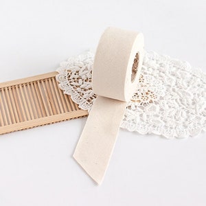 May include: A roll of beige masking tape with a partially unwound strip, resting on a white lace doily. A small, light brown bamboo tray is in the background. The tape roll is positioned at an angle, with the end of the tape pointing downwards.