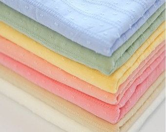 Pode incluir: Uma pilha de amostras de tecido em várias cores pastel, incluindo azul claro, verde, amarelo, rosa, bege e branco. O tecido tem um padrão texturizado sutil.