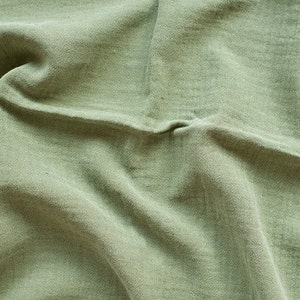 May include: A close-up of a green fabric with a wrinkled texture. The fabric is soft and has a natural look.