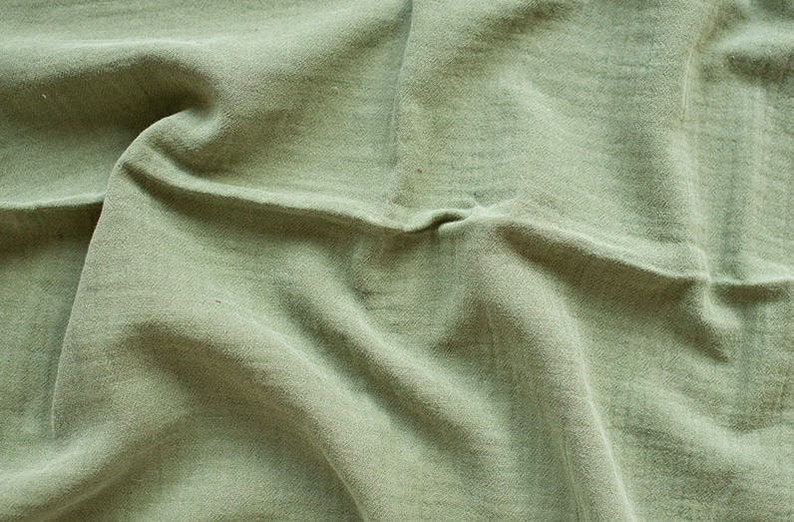 May include: A close-up of a green fabric with a wrinkled texture. The fabric is soft and has a natural look.