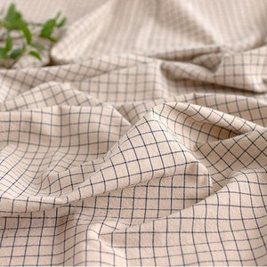 May include: Close-up of a beige fabric with a black grid pattern. The fabric is wrinkled and has a soft texture.