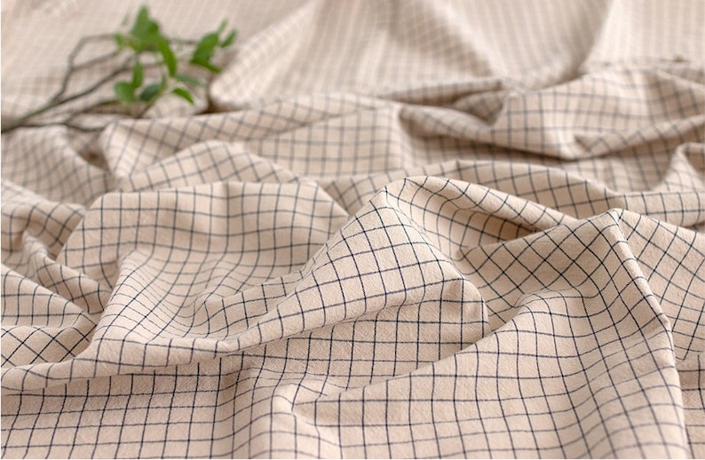 May include: Close-up of a beige fabric with a black grid pattern. The fabric is wrinkled and has a soft texture.