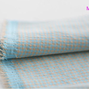 Pu&ograve; includere: Un pezzo di stoffa piegato con un motivo a quadri blu chiaro e beige. Il tessuto ha un bordo sfrangiato ed &egrave; etichettato "Mint Yellow".