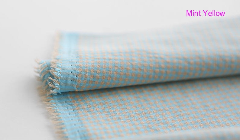 Pu&ograve; includere: Un pezzo di stoffa piegato con un motivo a quadri blu chiaro e beige. Il tessuto ha un bordo sfrangiato ed &egrave; etichettato "Mint Yellow".