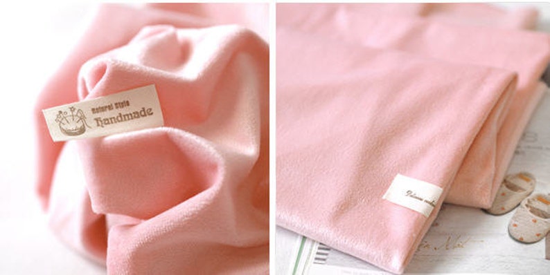 May include: Soft pink fabric with a velvety texture, possibly a blanket or cloth. The fabric is folded and has a small tag that reads "natural style handmade". The overall aesthetic is delicate and gentle.