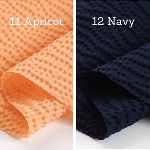 May include: Two fabric swatches, one apricot and one navy blue, each with a textured, dotted pattern. The apricot swatch is labeled "11 Apricot" and the navy swatch is labeled "12 Navy". The fabric is folded, showing the texture and color variations.