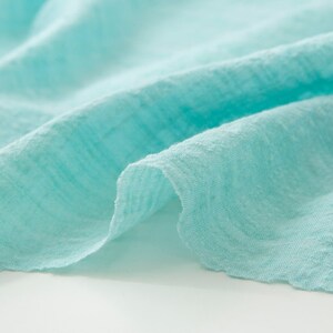 May include: Close-up of a light blue fabric with a textured surface. The fabric is soft and wrinkled, creating a relaxed and casual look.