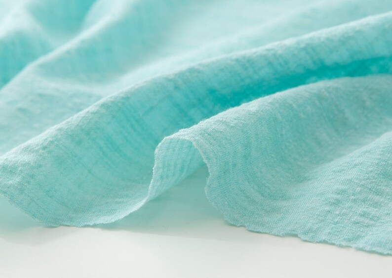 May include: Close-up of a light blue fabric with a textured surface. The fabric is soft and wrinkled, creating a relaxed and casual look.