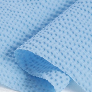May include: Close-up of a light blue, textured fabric with a waffle-like pattern. The fabric is folded, revealing layers and shadows. The material appears soft and lightweight, suitable for various applications.