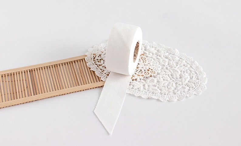 May include: A roll of white, textured paper with a cut edge, resting on a white lace doily. A small, light brown bamboo tray is to the left. The background is white.