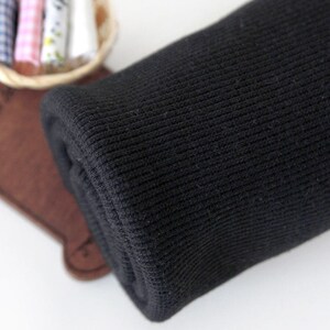 May include: Close-up of black ribbed fabric rolled up. The fabric has a soft, textured surface.