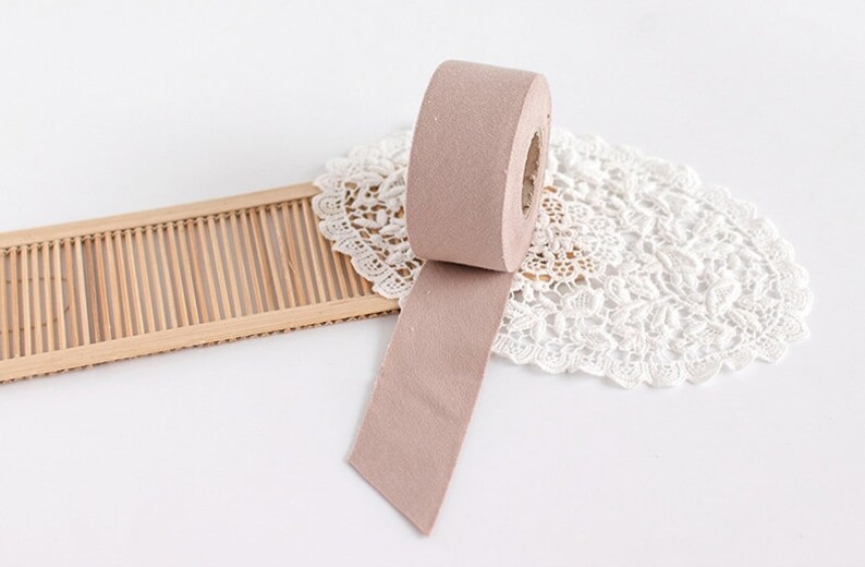 May include: A roll of light brown felt tape with a section unrolled, resting on a white lace doily. A small, rectangular wooden mat is to the left of the tape. The background is white.